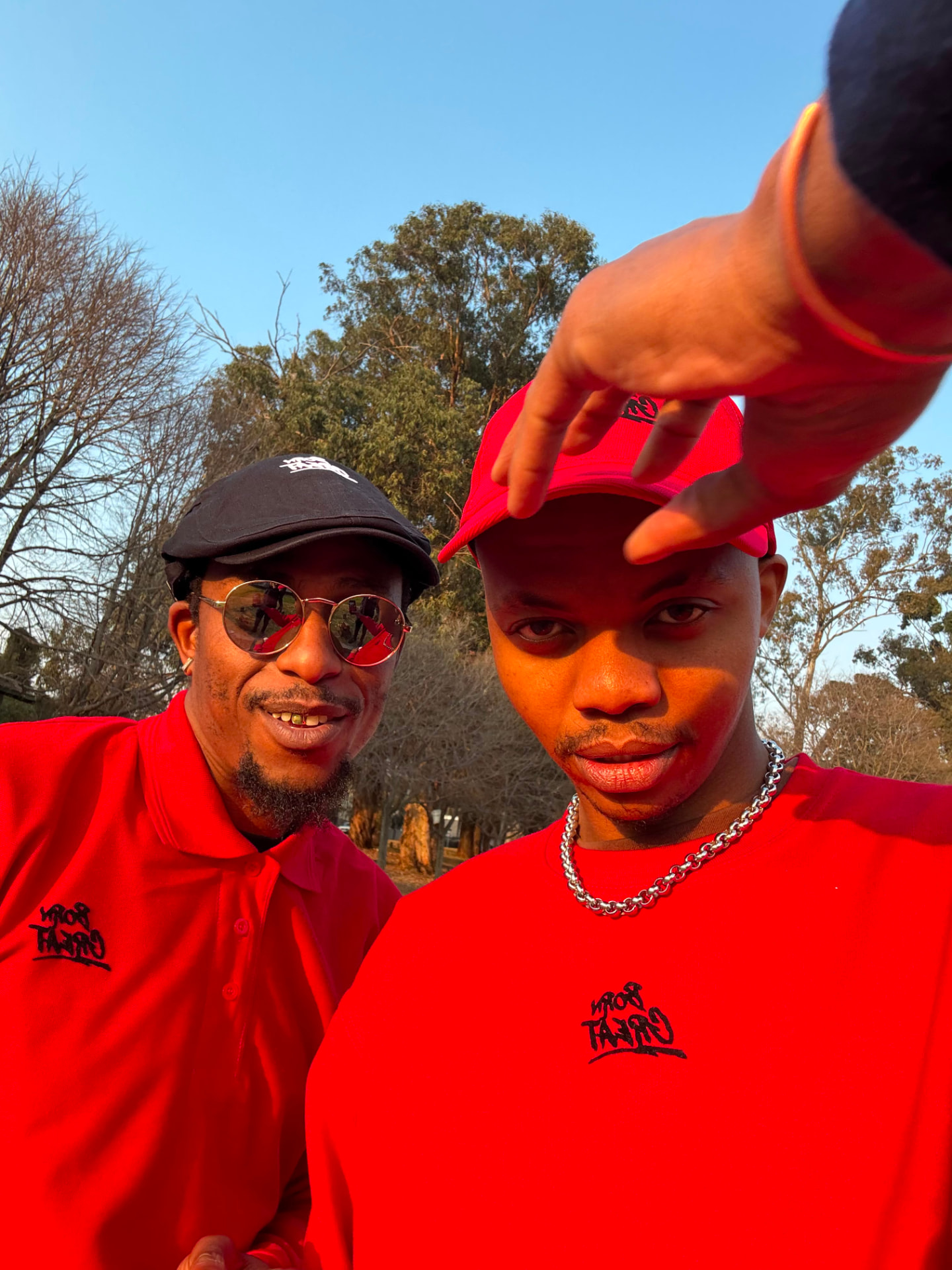 Two men in red Born Great polos and caps at golden hour